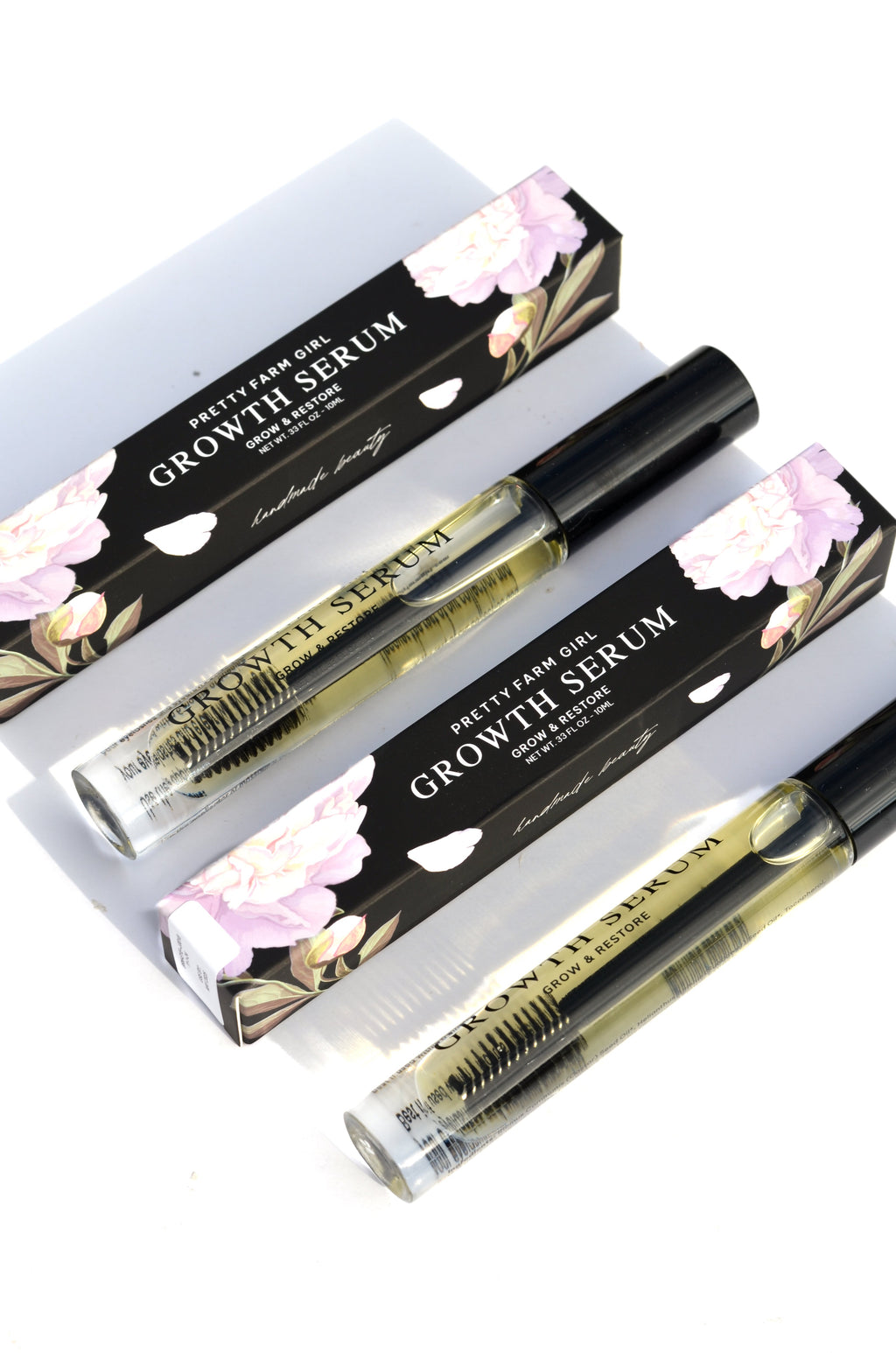 Three Eyelash + Eyebrow Growth Serum tubes, one resting across two open black floral-patterned boxes.