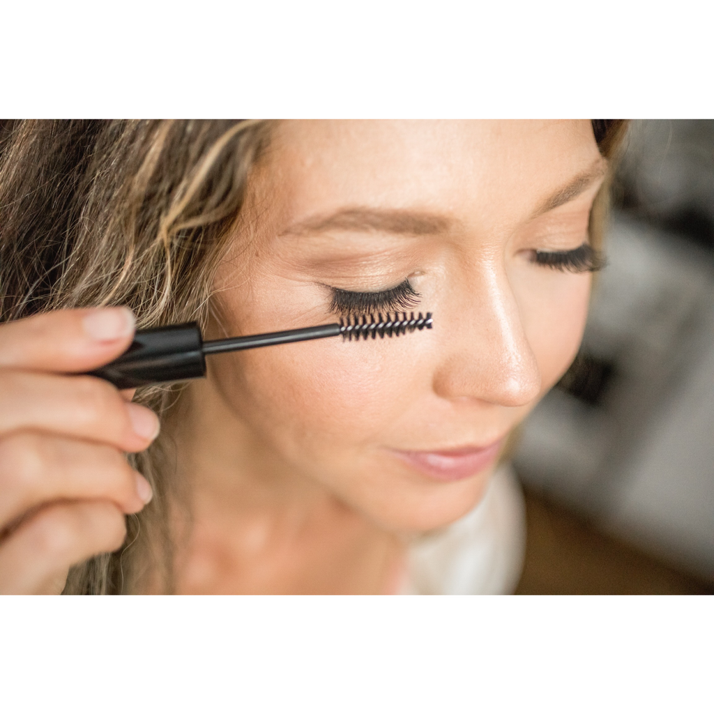 A woman brushes her upper lashes with a black spoolie for the Eyelash + Eyebrow Growth Serum.